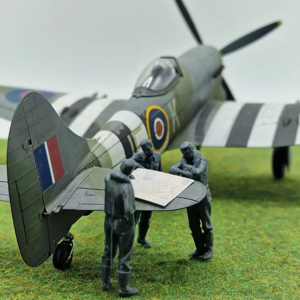 Model airplane with figures around a map on a grassy field