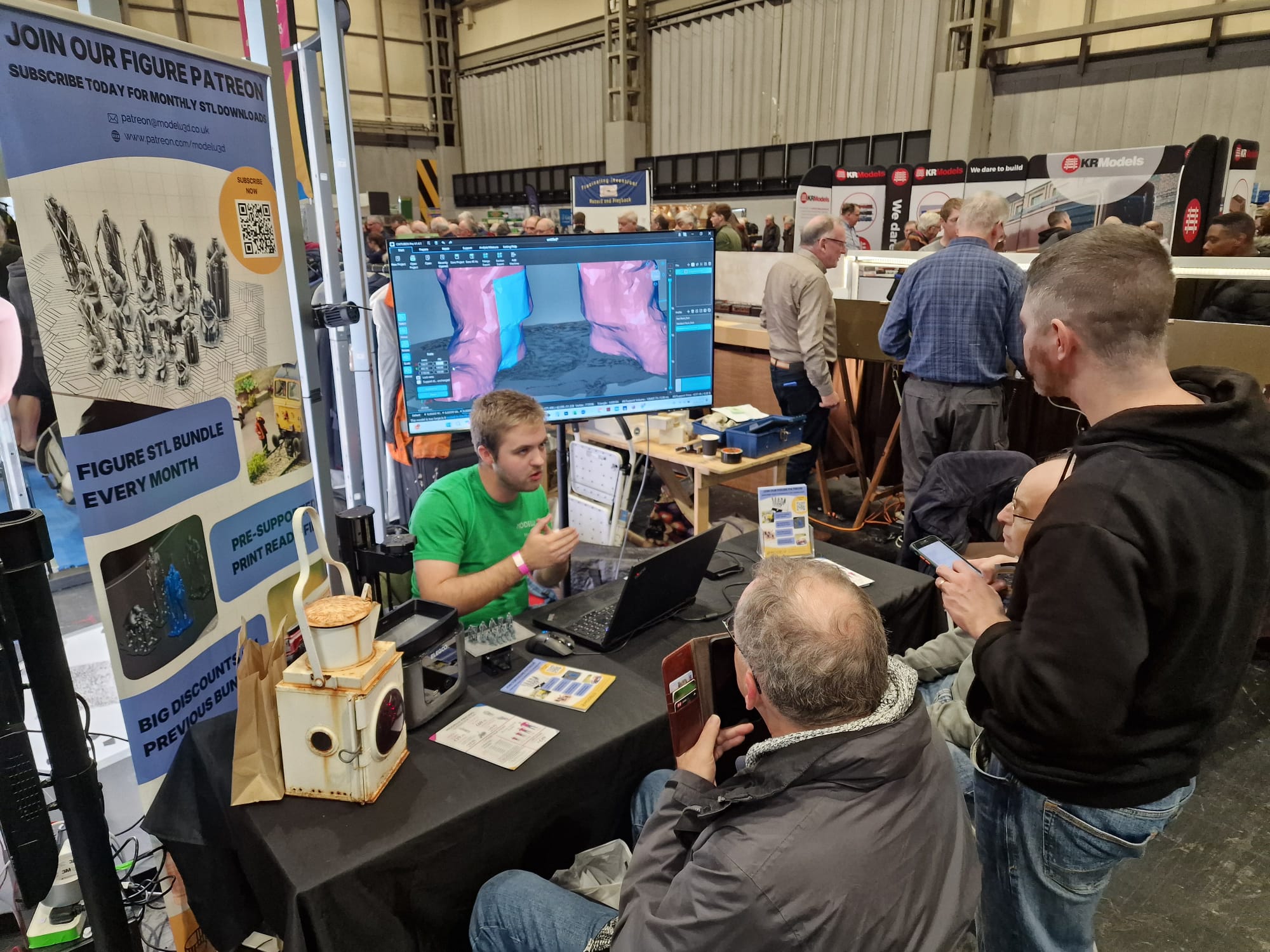 People interacting with a computer at a trade show booth with a large screen displaying a map.