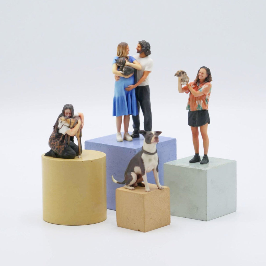 Figurines of people and a dog on geometric blocks against a white background