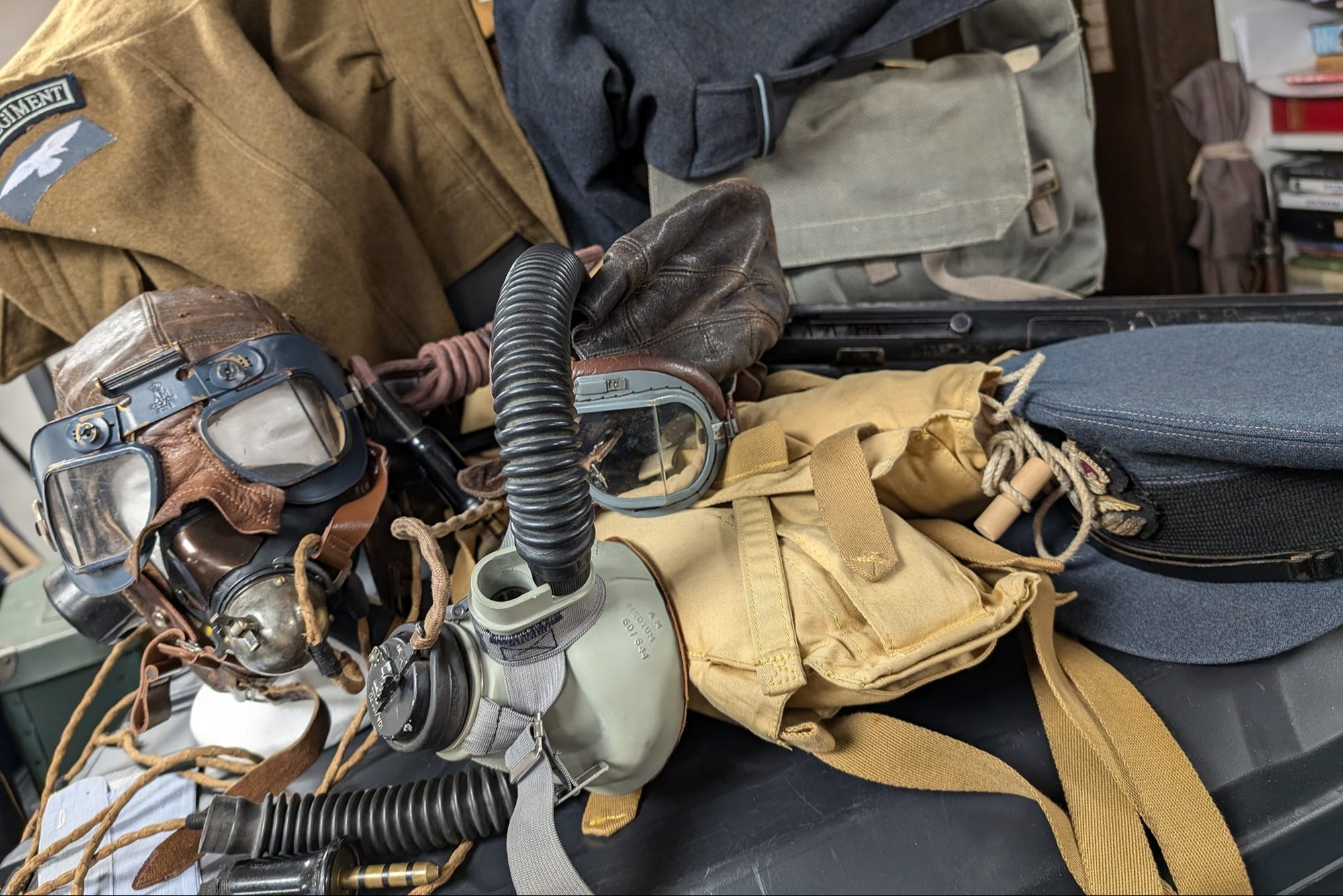 Vintage military equipment including goggles and gas mask on a suitcase.