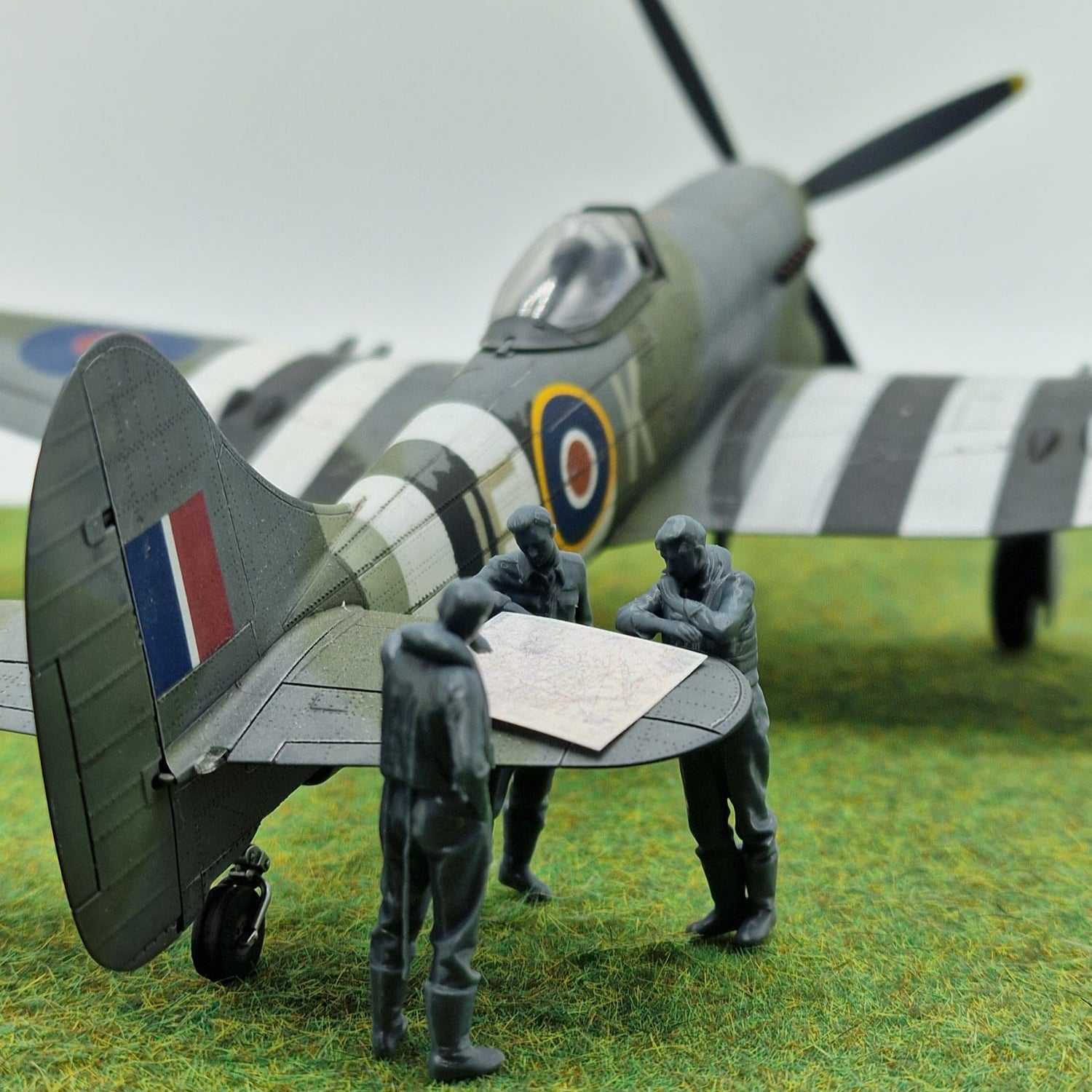 Model airplane with figures around a map on a grassy field